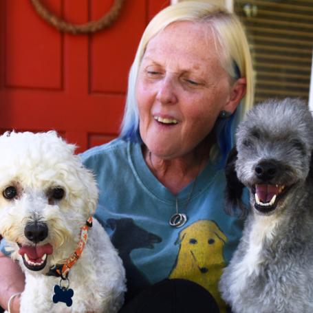 Smiling person sitting on the steps of a front porch with three dogs