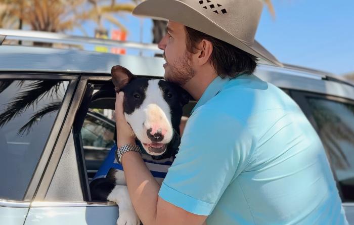Volunteer Steven Szydio hugging Chico the dog whose head is out a vehicle window