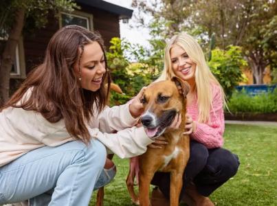 Two smiling people kneeling next to a dog in a yard