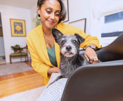 Smiling person petting a small dog on a hardwood floor in a living room