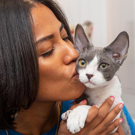 Woman holding and kissing the cheek of a gray and white cat