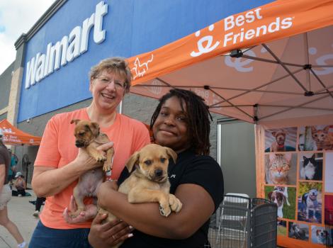 Two people holding puppies at a Best Friends adoption event in front of a Walmart store