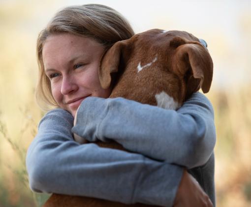 Person hugging a dog with her arms wrapped around the dog's neck