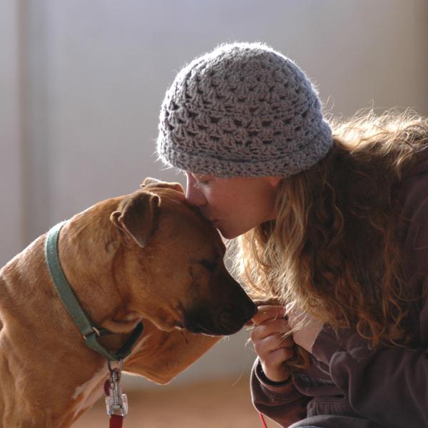 Best Friends employee Carissa kissing the top of Oscar's head, who is one of the Vicktory dogs