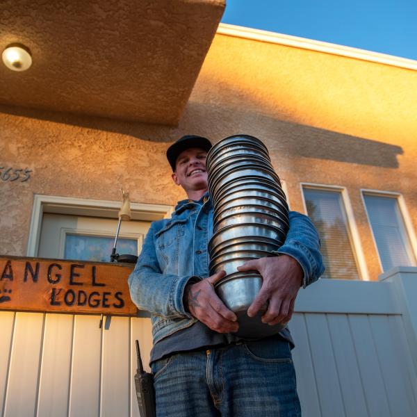 Smiling person holding a large stack of stainless steel dog bowls
