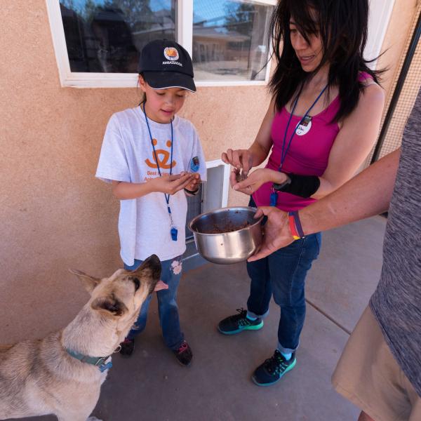 A few people with a bowl of food feeding a dog