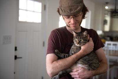 Person wearing a hat cradling a cat in his arms