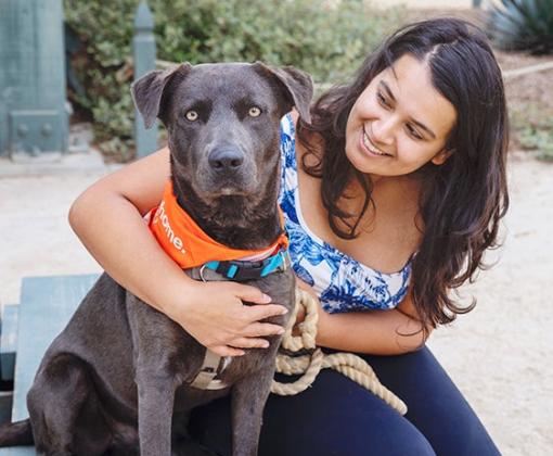 Smiling person outside with a leashed dog wearing a bandanna