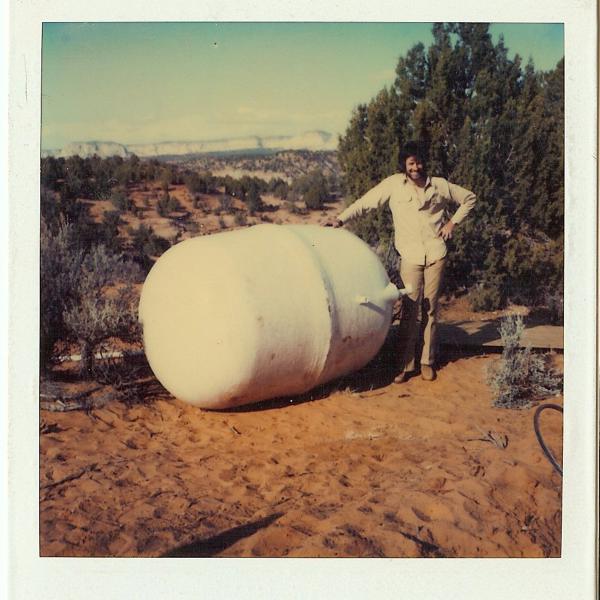 Co-founder Gregory Castle standing next to a water tank that will soon be buried near Angel Village, 1984.