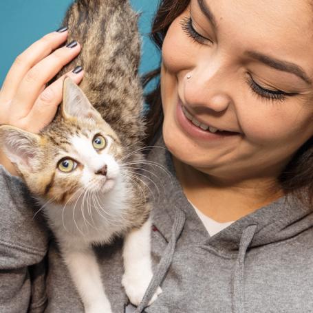 Woman holding tabby and white cat on shoulder