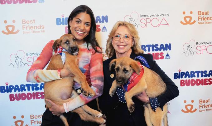 Two people holding puppies in front of a backdrop