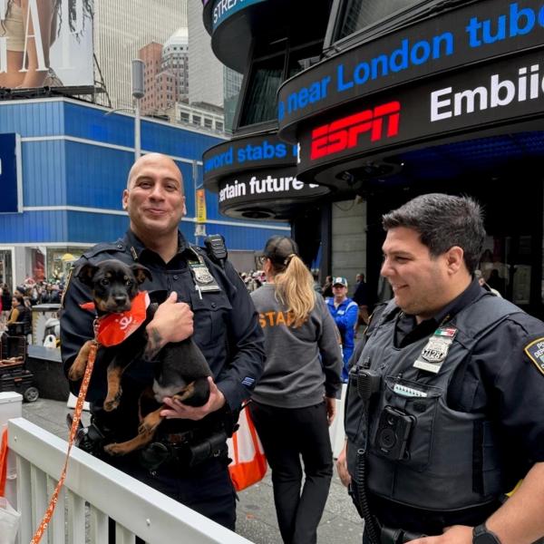 Oficial de policía de Nueva York sonriendo con un cachorro mientras otro oficial los mira