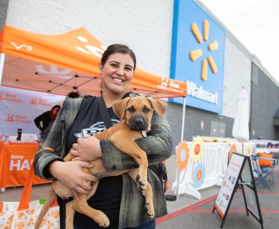 Person holding a puppy in front of a Best Friends canopy in front of a Walmart store