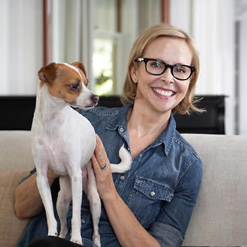 Lona Williams sitting on couch holding small white and brown dog