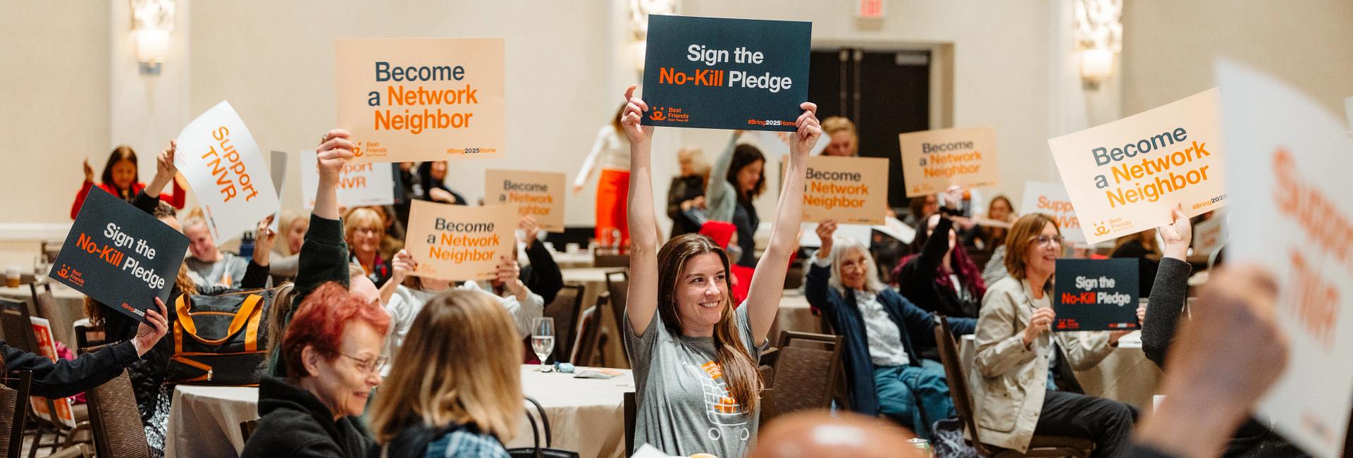 Attendees of the Chicago Bring No-Kill Home Summit smiling and holding up signs that say "Support TNVR", "Become a Network Neighbor", etc.