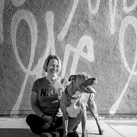 Woman with large dog sitting on sidewalk in front of mural
