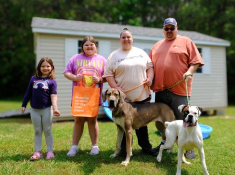 Four people with two dogs on leashes in front of a shed