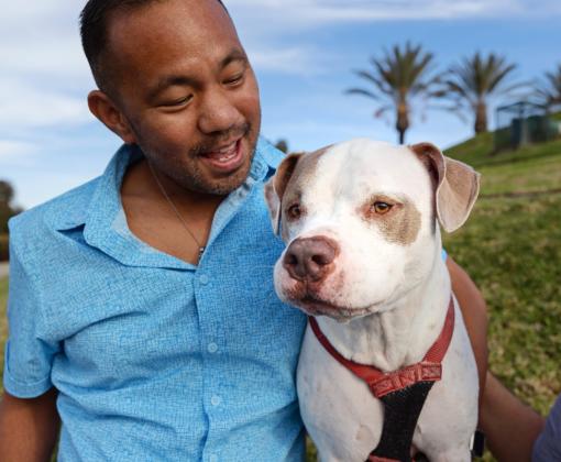 Person smiling at a dog they're sitting next to on the grass