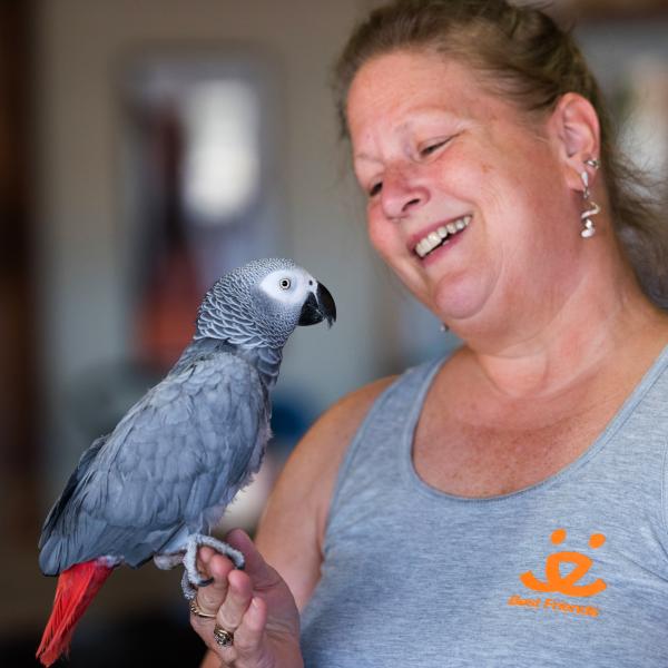Smiling person wearing a Best Friends tank top holding an African grey parrot