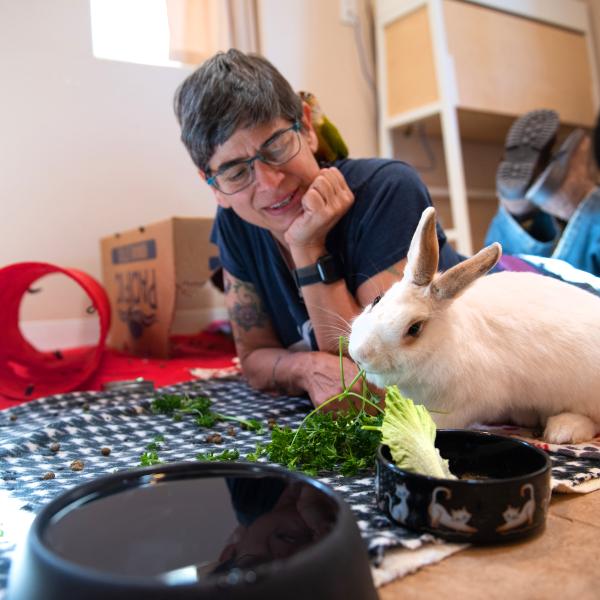 Smiling person lying on the ground with a rabbit who is eating greens