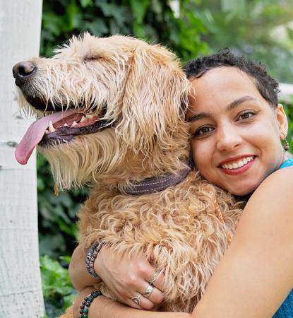 Person hugging a large, tan dog, outside on a lawn