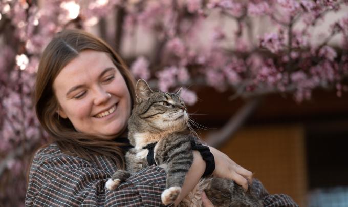 Caregiver Ashley McDaniel holding a cat in front of a flowering tree