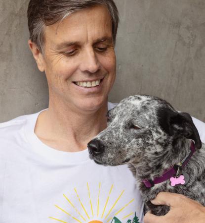 Smiling person sitting outside against a cement wall with a dog