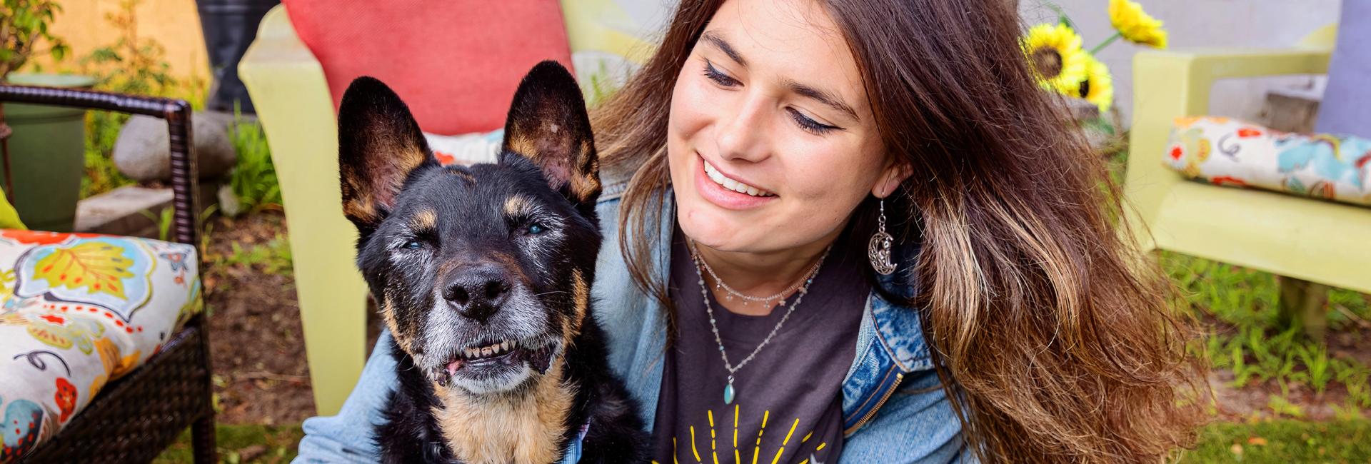 Smiling person sitting on the grass with a senior dog